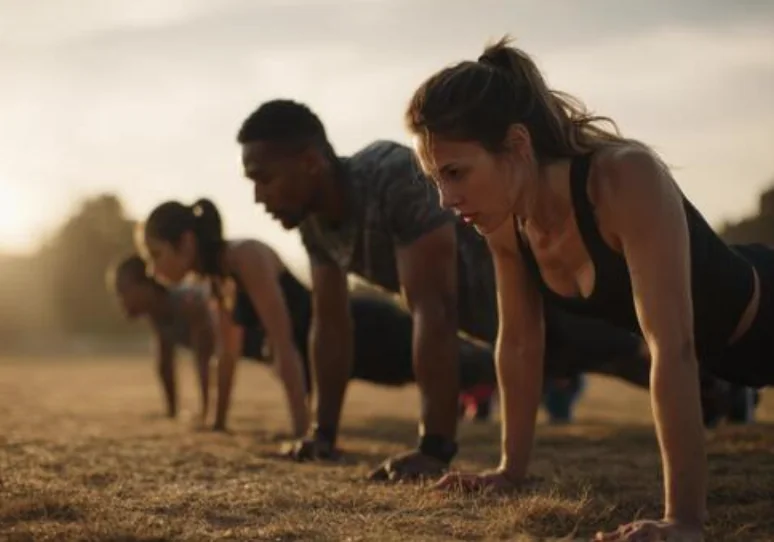 Group training together outdoors at sunrise, holding a press-up position
